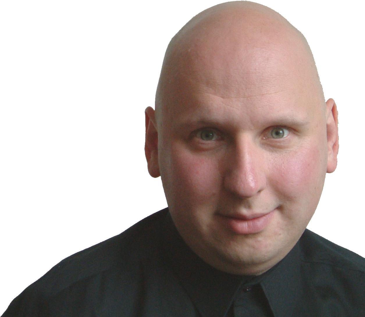 Ein glatzköpfiger Mann mit schwarzem Hemd, der leicht lächelnd in die Kamera schaut, vor einem weißen Hintergrund.